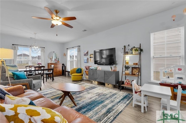 living room featuring ceiling fan with notable chandelier and light wood-type flooring