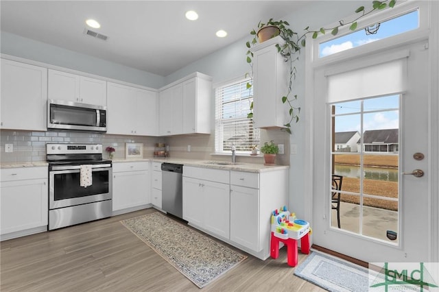 kitchen with sink, appliances with stainless steel finishes, white cabinetry, backsplash, and light hardwood / wood-style floors