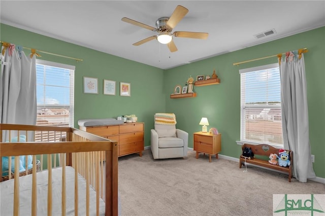 bedroom with a nursery area, light colored carpet, ceiling fan, and multiple windows