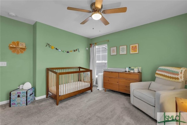 carpeted bedroom featuring a nursery area and ceiling fan