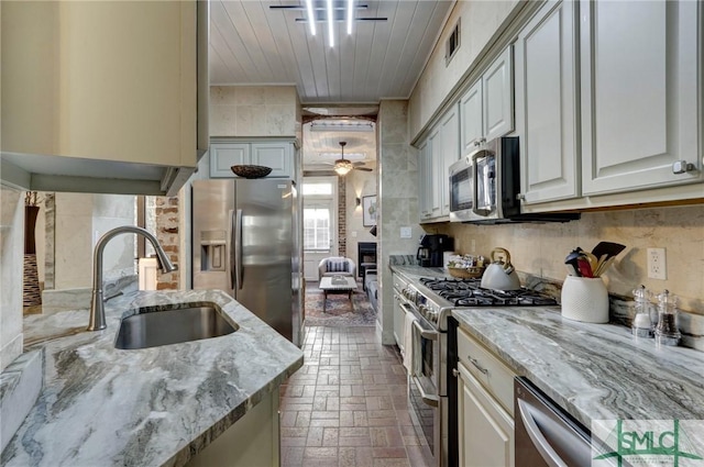 kitchen featuring ceiling fan, appliances with stainless steel finishes, sink, light stone countertops, and a large fireplace