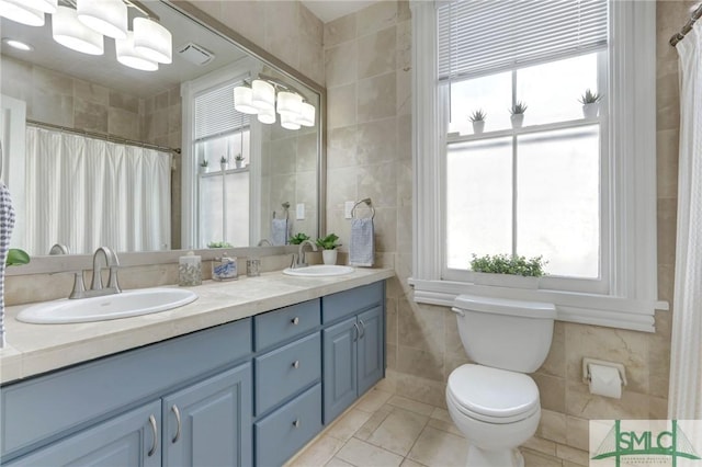 bathroom with toilet, tile patterned flooring, vanity, and tile walls