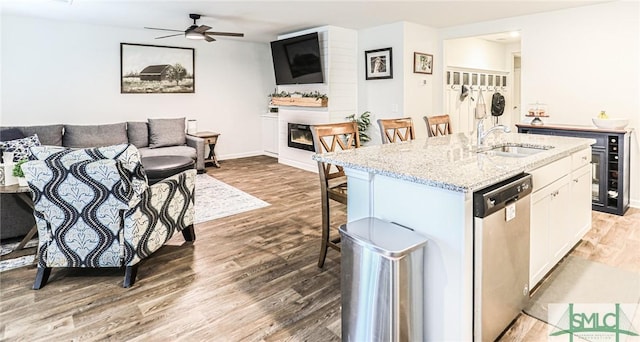 kitchen featuring light stone countertops, white cabinets, an island with sink, sink, and stainless steel dishwasher