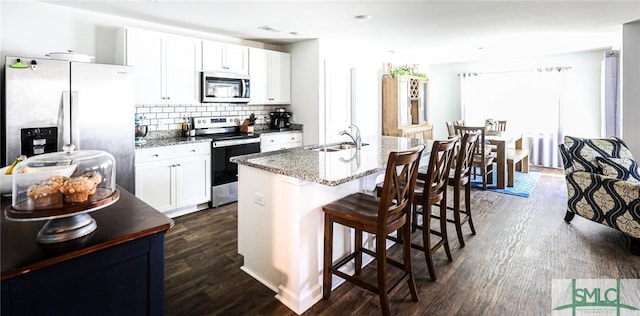 kitchen with white cabinets, stainless steel appliances, tasteful backsplash, an island with sink, and stone countertops