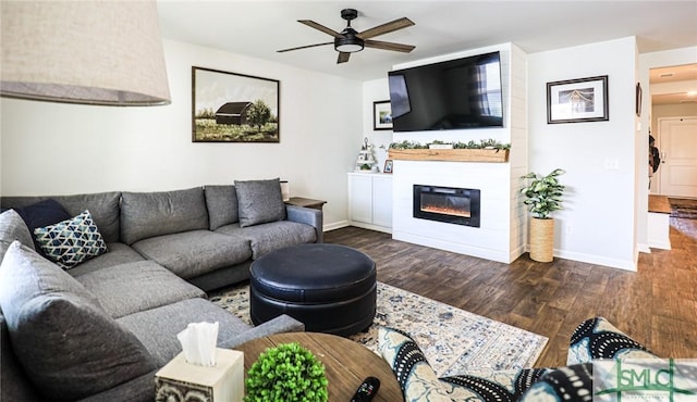 living room featuring ceiling fan, dark wood-type flooring, and a large fireplace