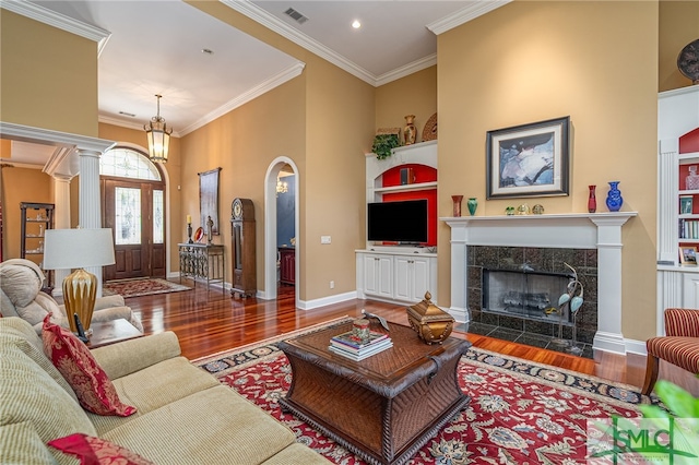 living room featuring a high ceiling, wood-type flooring, a fireplace, built in features, and crown molding