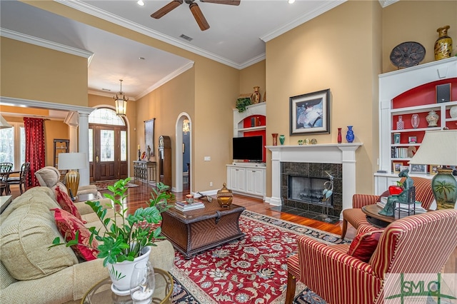 living room featuring wood-type flooring, crown molding, ornate columns, built in shelves, and a fireplace