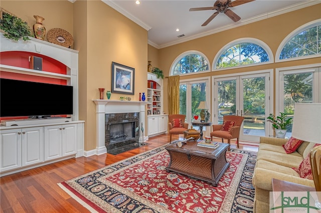 living room with ceiling fan, light wood-type flooring, built in shelves, a fireplace, and ornamental molding