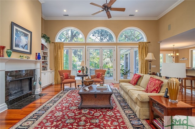 living room with crown molding, a fireplace, hardwood / wood-style flooring, built in features, and ceiling fan with notable chandelier