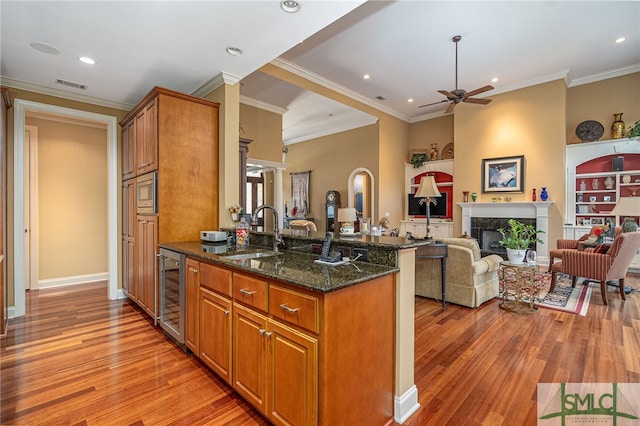 kitchen featuring a fireplace, sink, ornamental molding, dark stone counters, and beverage cooler