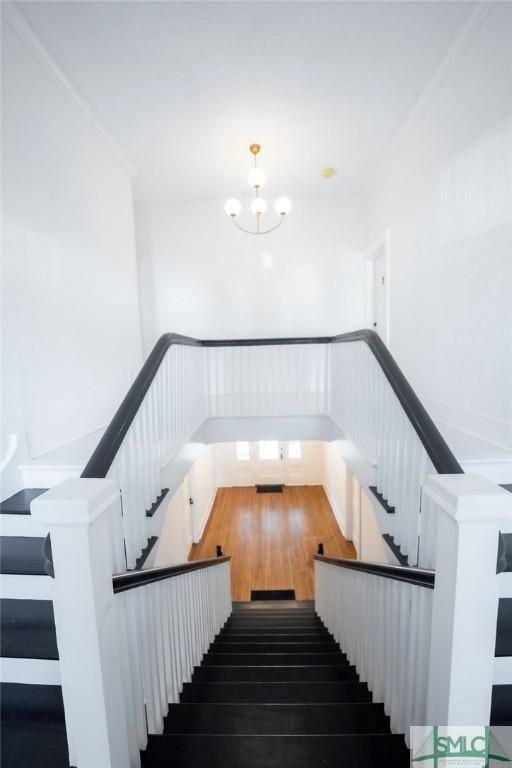 stairs featuring hardwood / wood-style flooring, ornamental molding, and an inviting chandelier