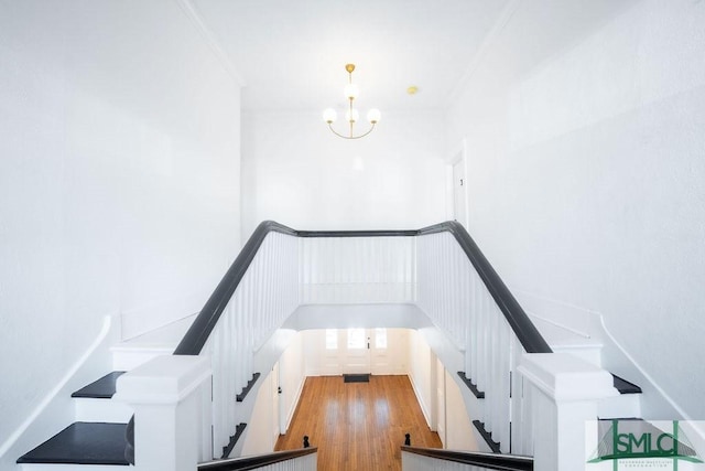 staircase featuring hardwood / wood-style flooring, crown molding, and an inviting chandelier