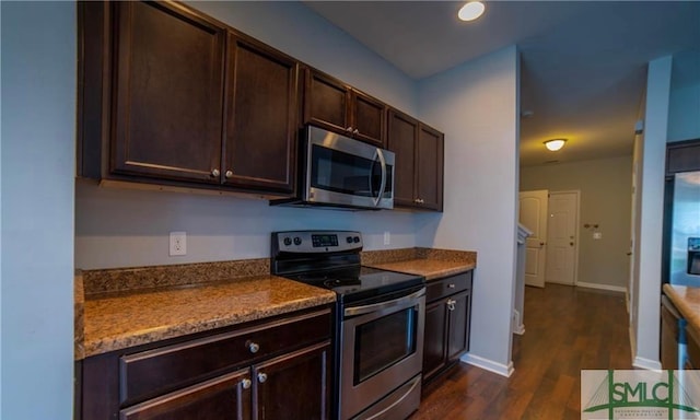 kitchen featuring light stone countertops, dark brown cabinets, dark hardwood / wood-style flooring, and stainless steel appliances