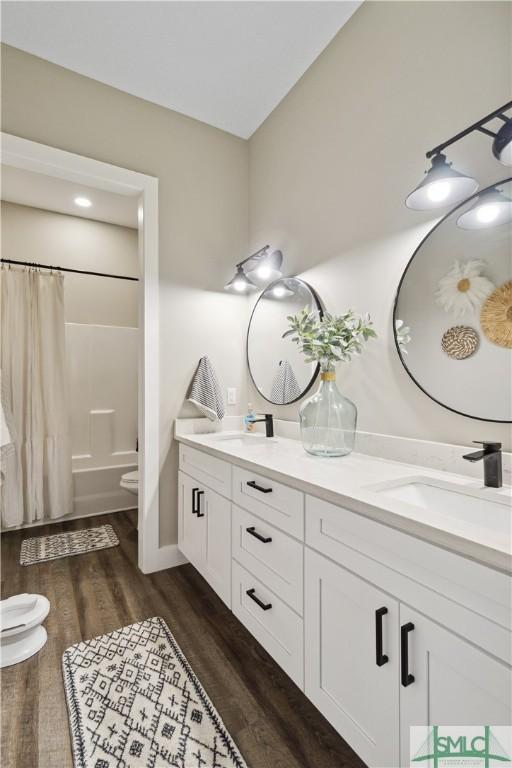 bathroom featuring wood finished floors, double vanity, a sink, toilet, and shower / tub combo with curtain