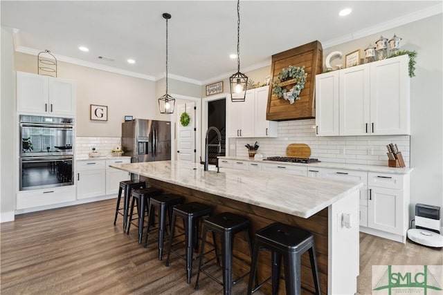 kitchen featuring appliances with stainless steel finishes, white cabinets, tasteful backsplash, a kitchen island with sink, and a breakfast bar