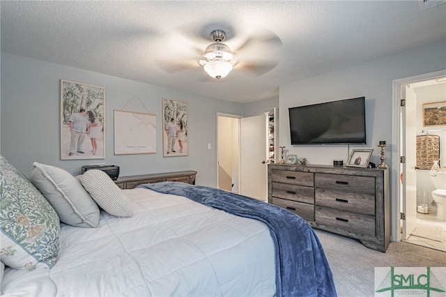 bedroom featuring ceiling fan, a textured ceiling, light carpet, and ensuite bath