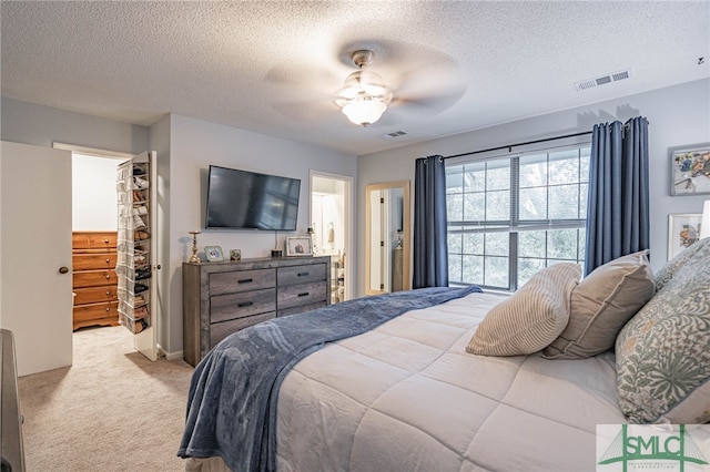 carpeted bedroom with a textured ceiling, a closet, ceiling fan, and a walk in closet