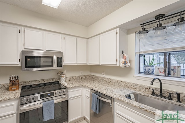 kitchen featuring light stone countertops, a textured ceiling, white cabinets, appliances with stainless steel finishes, and sink