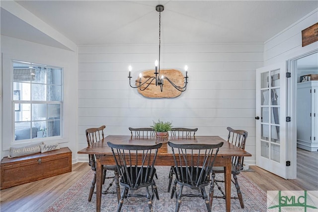 dining space featuring wood-type flooring, wood walls, and an inviting chandelier