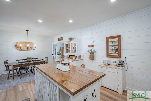 kitchen featuring white cabinets, a kitchen island, decorative light fixtures, wood walls, and light hardwood / wood-style flooring