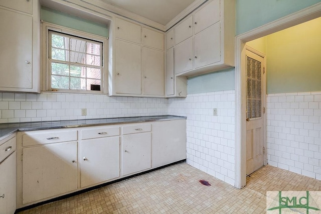 kitchen with light tile patterned floors, white cabinetry, crown molding, and tile walls