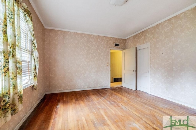 empty room featuring hardwood / wood-style floors, ornamental molding, and a healthy amount of sunlight