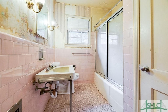 bathroom featuring tile patterned floors, bath / shower combo with glass door, toilet, and tile walls