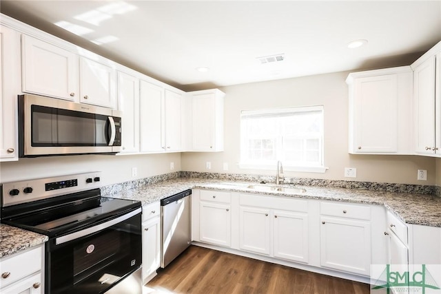 kitchen with dark wood-style floors, stainless steel appliances, visible vents, white cabinetry, and a sink