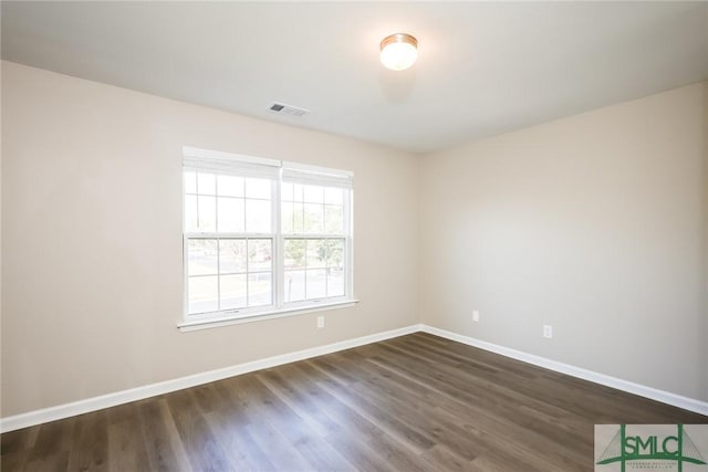 unfurnished room with visible vents, dark wood finished floors, and baseboards