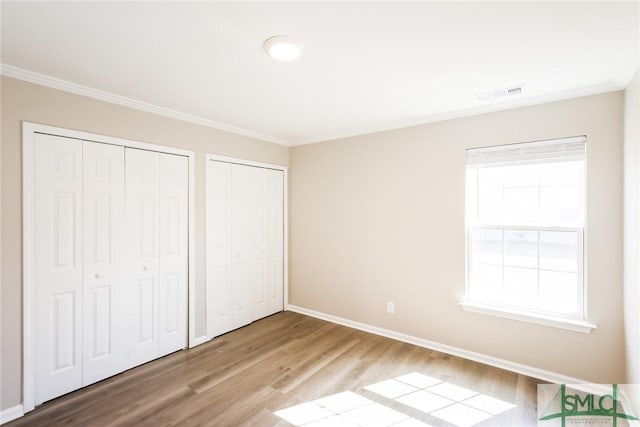 unfurnished bedroom with wood finished floors, visible vents, baseboards, and two closets