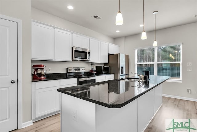 kitchen with pendant lighting, appliances with stainless steel finishes, white cabinetry, sink, and a kitchen island with sink