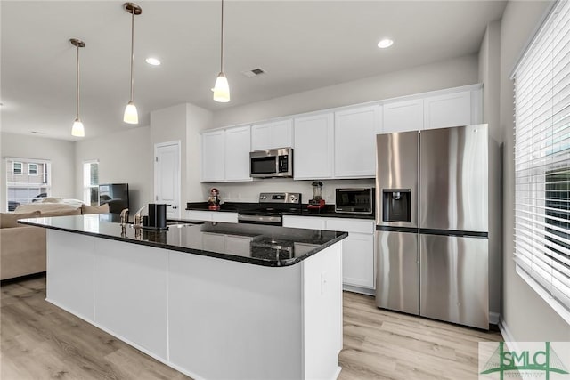 kitchen with decorative light fixtures, white cabinets, a kitchen island with sink, and stainless steel appliances