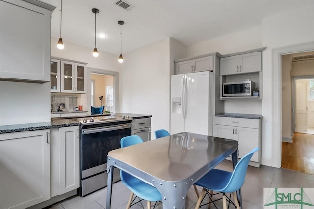 kitchen featuring pendant lighting, appliances with stainless steel finishes, a kitchen bar, dark stone counters, and gray cabinetry