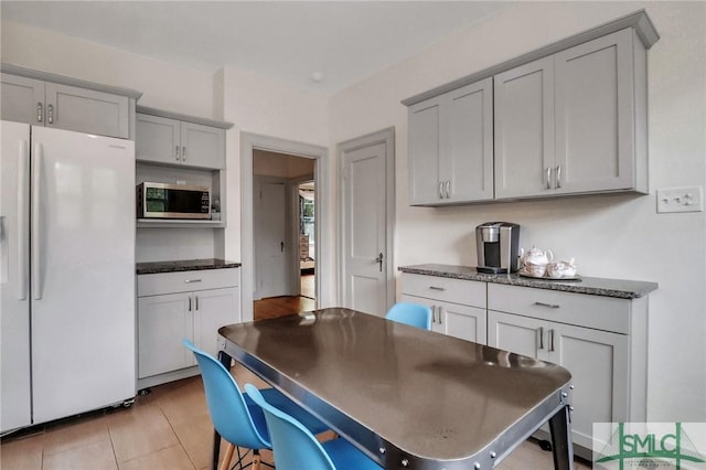 kitchen with white fridge with ice dispenser, dark stone countertops, gray cabinetry, and light tile patterned flooring