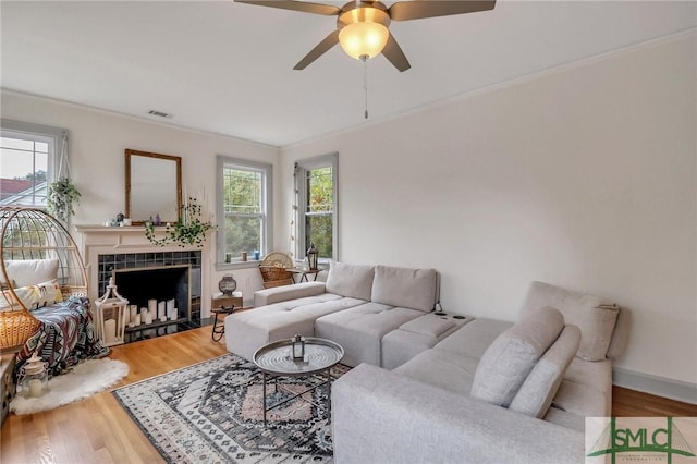 living room featuring wood-type flooring, a tile fireplace, a healthy amount of sunlight, and ornamental molding