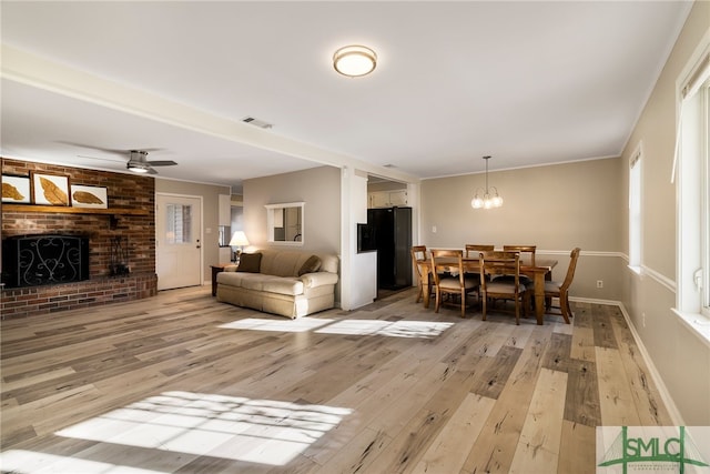 living room featuring ceiling fan with notable chandelier, light wood-type flooring, crown molding, and a fireplace