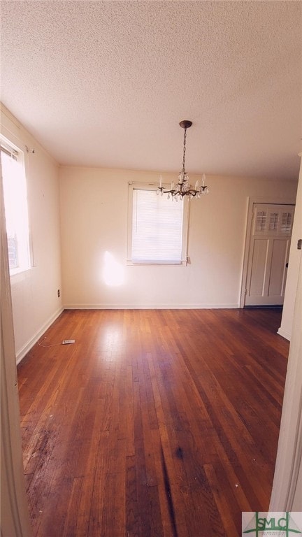 unfurnished dining area featuring dark wood-type flooring, a textured ceiling, and a notable chandelier