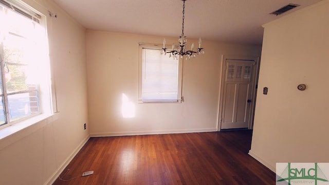 unfurnished dining area featuring dark wood-type flooring and an inviting chandelier