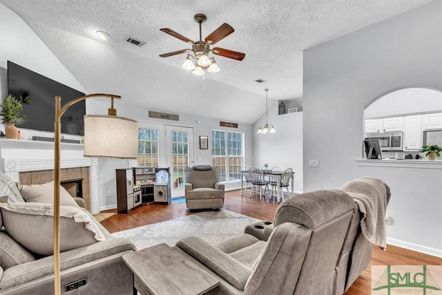 living room featuring lofted ceiling, wood-type flooring, a textured ceiling, ceiling fan, and a fireplace