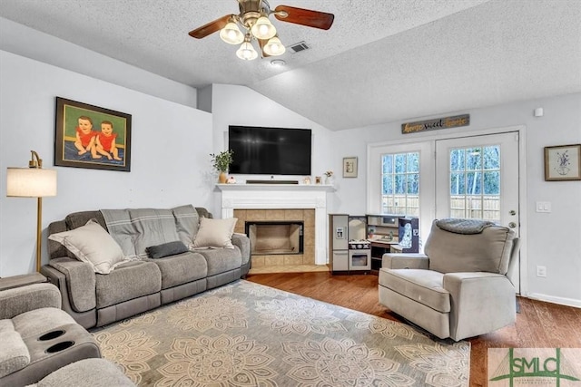 living room featuring hardwood / wood-style flooring, ceiling fan, a fireplace, and vaulted ceiling