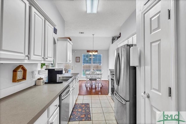 kitchen featuring lofted ceiling, white cabinetry, light tile patterned floors, pendant lighting, and stainless steel appliances