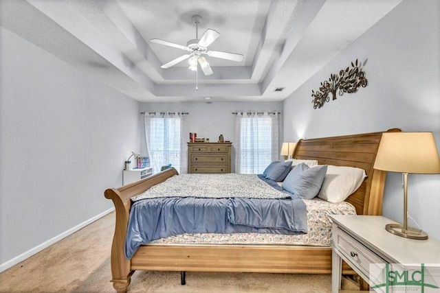 carpeted bedroom with ceiling fan and a tray ceiling