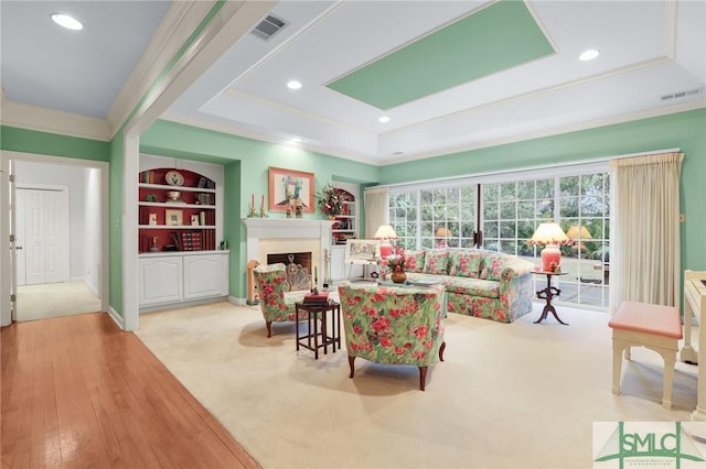 living room featuring a tray ceiling, ornamental molding, built in features, and light colored carpet