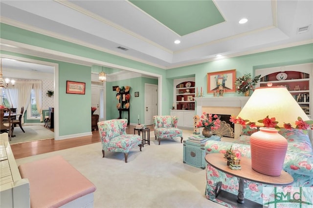 carpeted living room with built in shelves, ornamental molding, a raised ceiling, and a chandelier