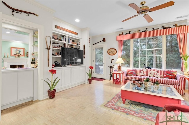 living room with ceiling fan, built in shelves, ornamental molding, and light parquet floors