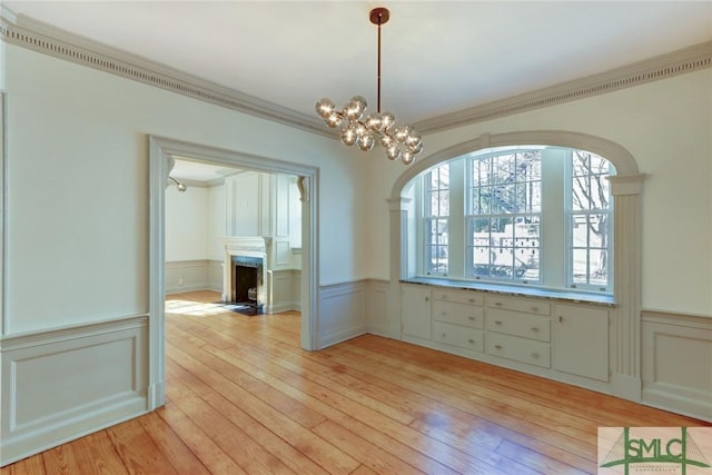 unfurnished dining area featuring crown molding, an inviting chandelier, and light wood-type flooring