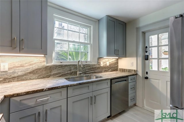 kitchen featuring sink, gray cabinetry, stone counters, stainless steel appliances, and decorative backsplash