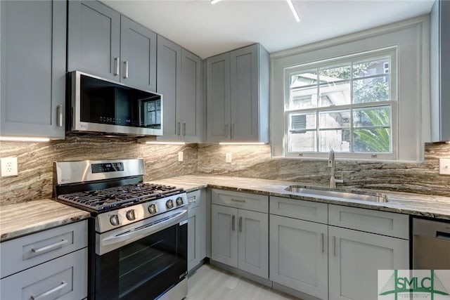 kitchen with gray cabinets, appliances with stainless steel finishes, tasteful backsplash, sink, and light stone countertops