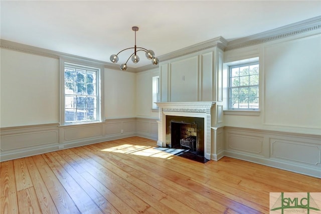 unfurnished living room featuring an inviting chandelier, light hardwood / wood-style flooring, and ornamental molding