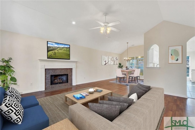 living room featuring a tiled fireplace, vaulted ceiling, dark hardwood / wood-style floors, and ceiling fan with notable chandelier